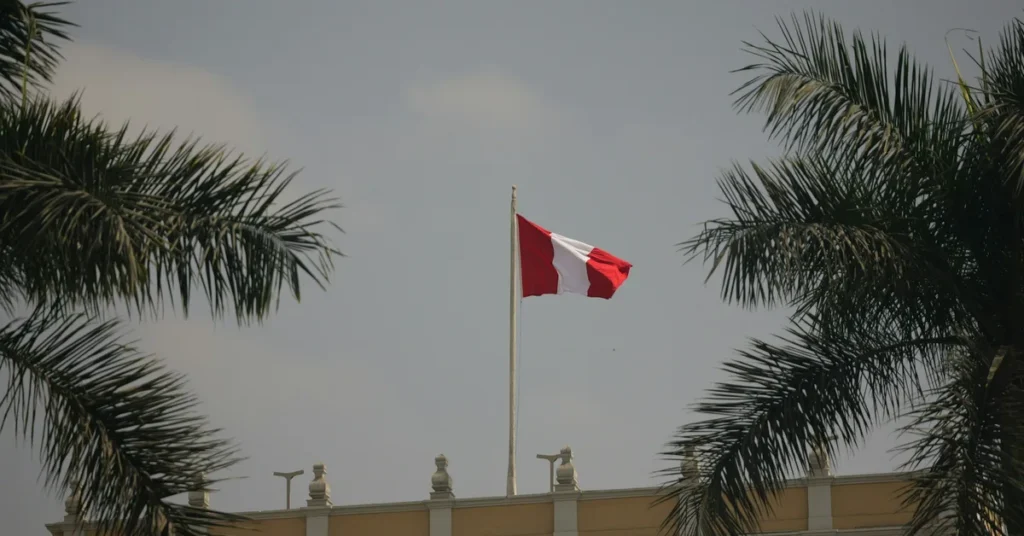 Bandera de Perú en lo alto de un edificio, entre palmeras