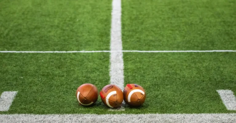 Tres balones de fútbol americano sobre el césped junto a la línea de la yarda 50